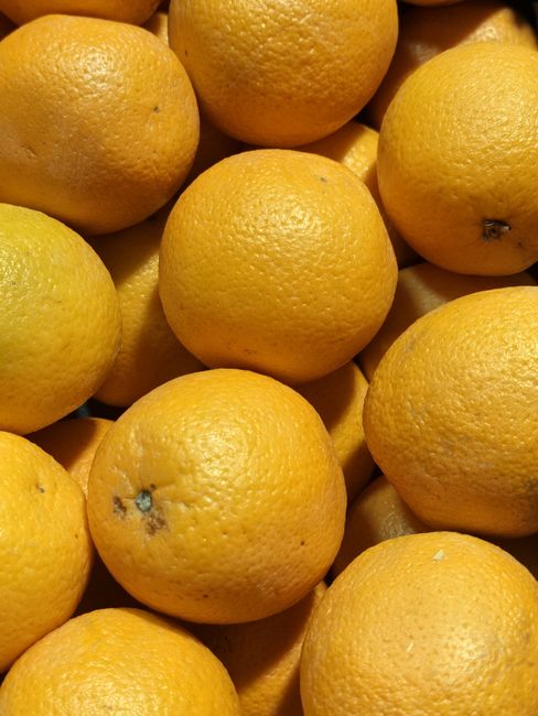 Close-up image showing a collection of fresh, ripe oranges with bright orange, textured skins. The oranges are piled together, occupying the foreground of the image, with their varying sizes and minor surface imperfections such as small blemishes and spots visible. The lighting is even, highlighting the natural color and surface texture of the fruit. In the background, additional oranges are partially visible, creating a sense of abundance. The scene appears to be set outdoors or in a market environment, typical for fresh produce displays, but no additional contextual elements such as baskets or crates are present. This detailed visual focus on the oranges emphasizes their vibrant colour and textured skin, aligning with themes of fresh fruit and natural produce, which could be associated with local markets or food-related waste and recycling services, similar to the offerings of House Clearance Ealing in managing waste from fruit and produce remains in food preparation or grocery contexts.