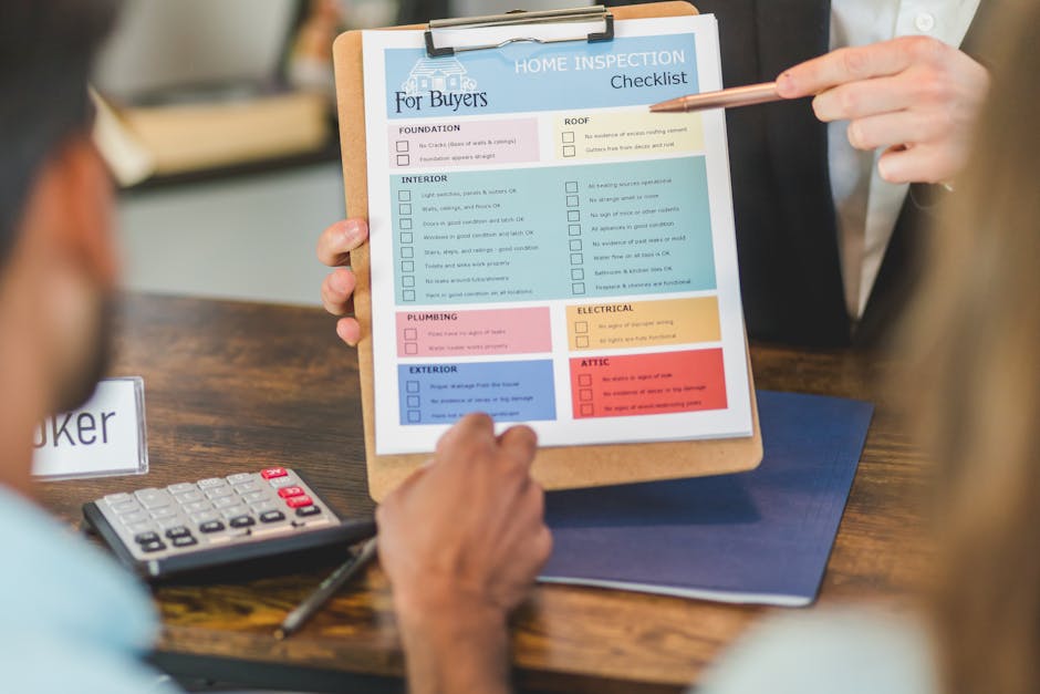 A person holding a clipboard with a home inspection checklist displayed prominently on a wooden table. The checklist includes categories such as foundation, roof, interior, exterior, plumbing, electrical, and attic, each with checkboxes and color-coded sections in pink, yellow, blue, and red. The individual is pointing at the checklist with a light pink pencil, while another person, partially visible, rests their arm near a calculator with red and white buttons. The background is slightly blurred, indicating an indoor setting, possibly an office or consultation space, with a neutral color palette and soft lighting. The scene suggests a professional assessment related to property condition, which may be a step before organising an independent rubbish or waste collection service through companies like House Clearance Ealing, particularly for estate clearance or home renovation waste removal.